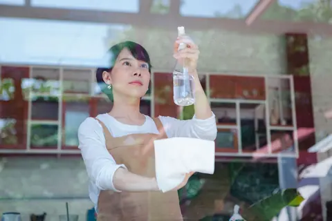 A woman spraying cleaner onto a window pane, holding a folded cloth