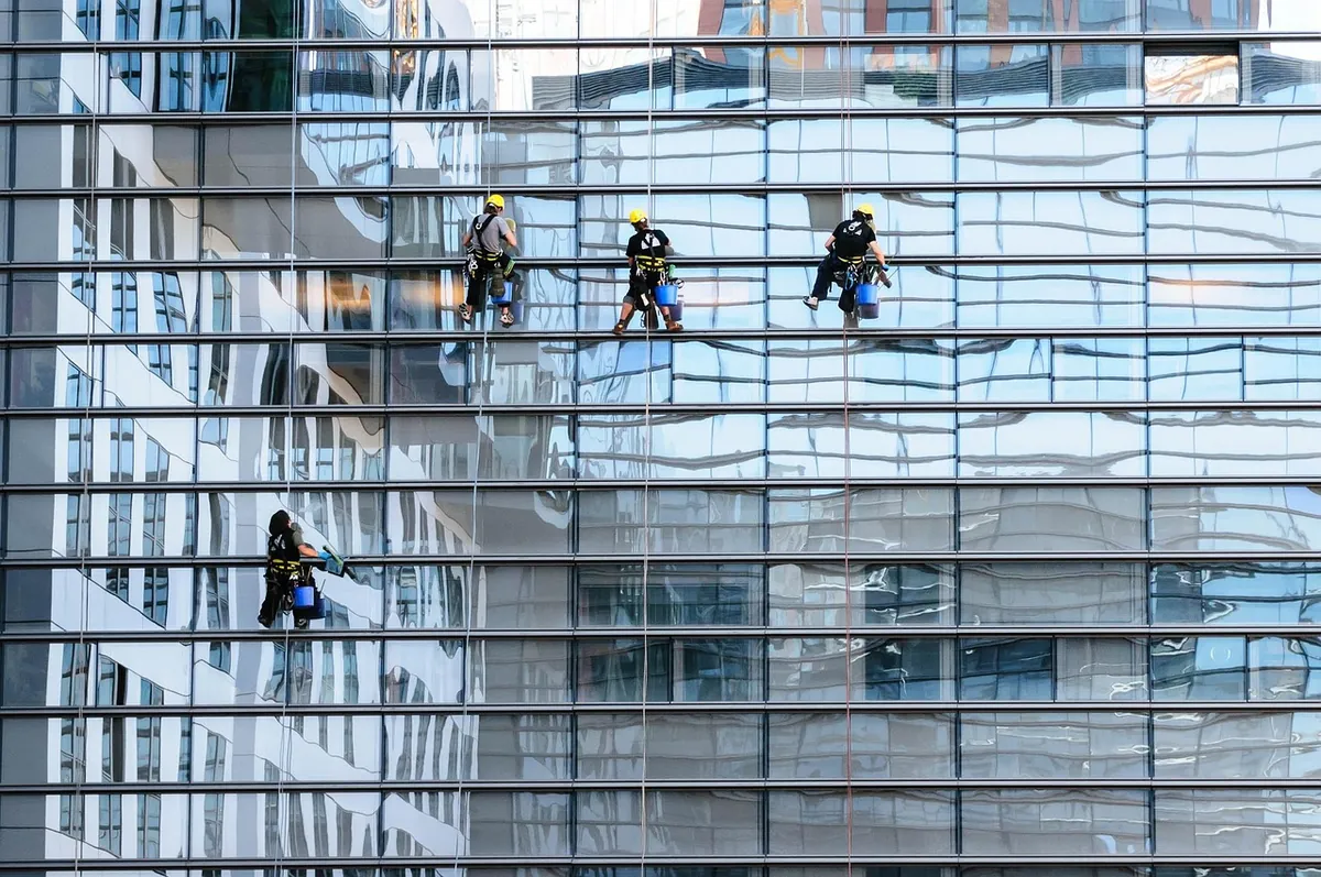 Rope-access window cleaners suspended against the glass facade of a skyscraper