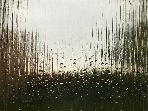 Condensation fogging a pane of glass with droplets forming, the humid environment that drives shower glass corrosion