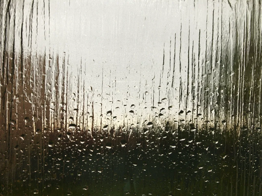 Condensation fogging a pane of glass with droplets forming, the humid environment that drives shower glass corrosion
