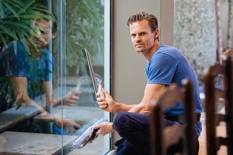 A person washing a large pane of glass with a squeegee, mid-stroke