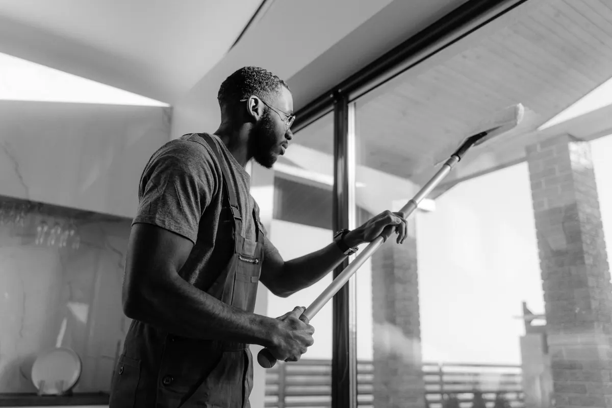 A window cleaner working a tall pane with a squeegee on an extension pole