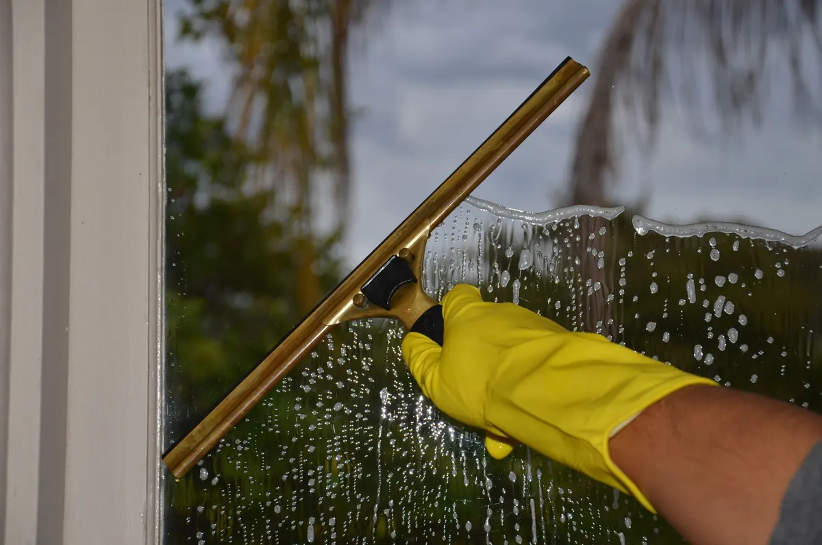 A gloved hand drawing a squeegee down a wet window