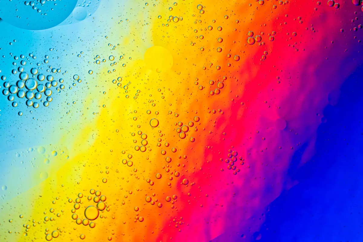 A vivid rainbow oil-film sheen spread across a surface, like outgassing residue on glass