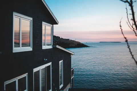 A dark coastal home with large windows overlooking the sea, exposed to salt air