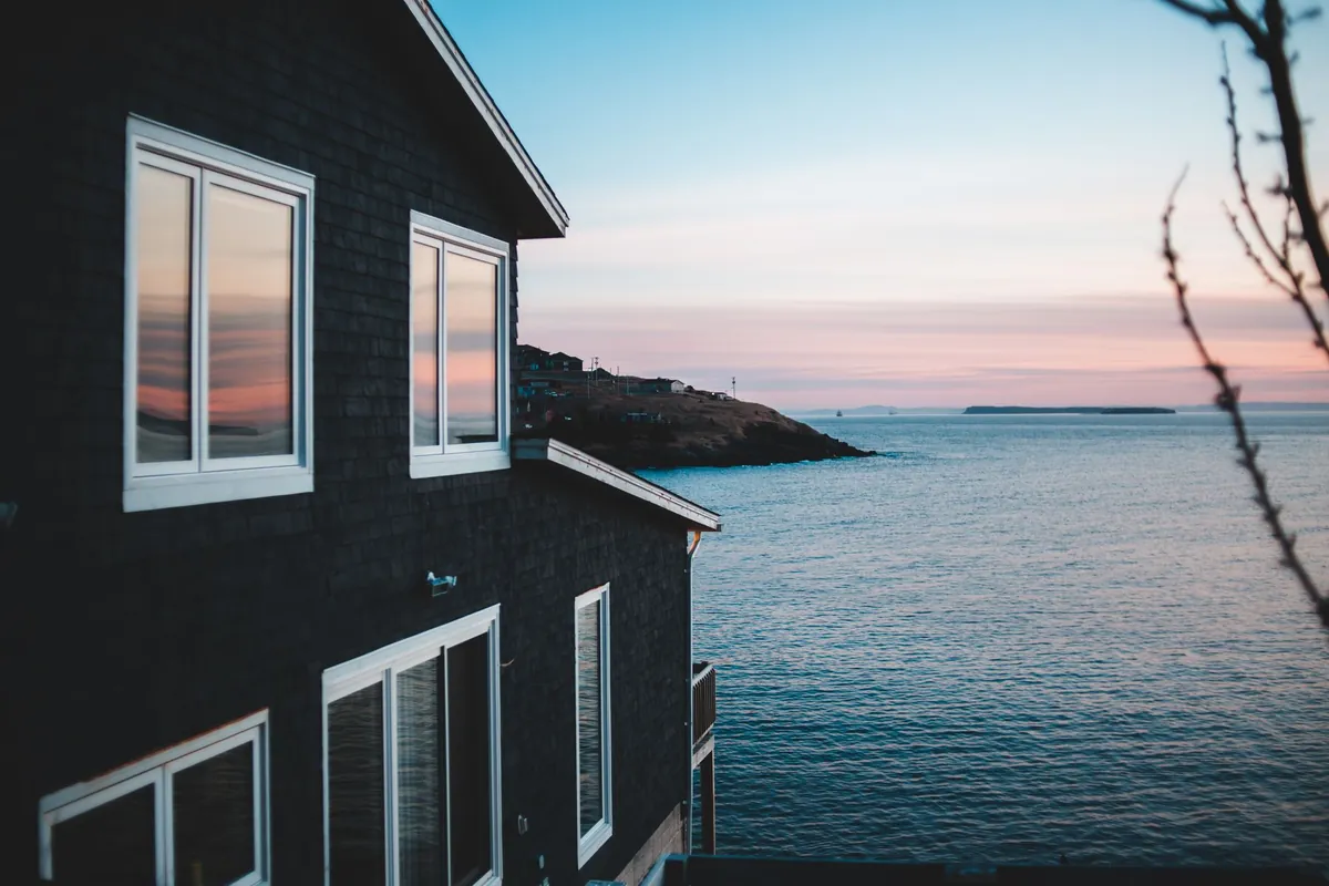 A dark coastal home with large windows overlooking the sea, exposed to salt air