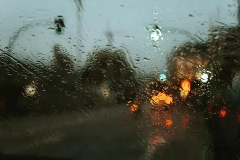 Rain-streaked window glass with blurred light beyond, showing smears that appear after cleaning