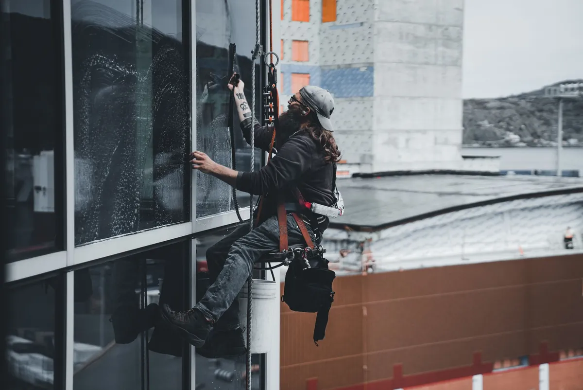 A rope-access worker suspended high on the glass face of a tall building