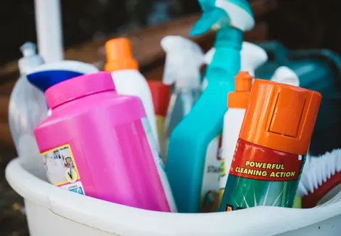 A tub crowded with household cleaning sprays and bottles