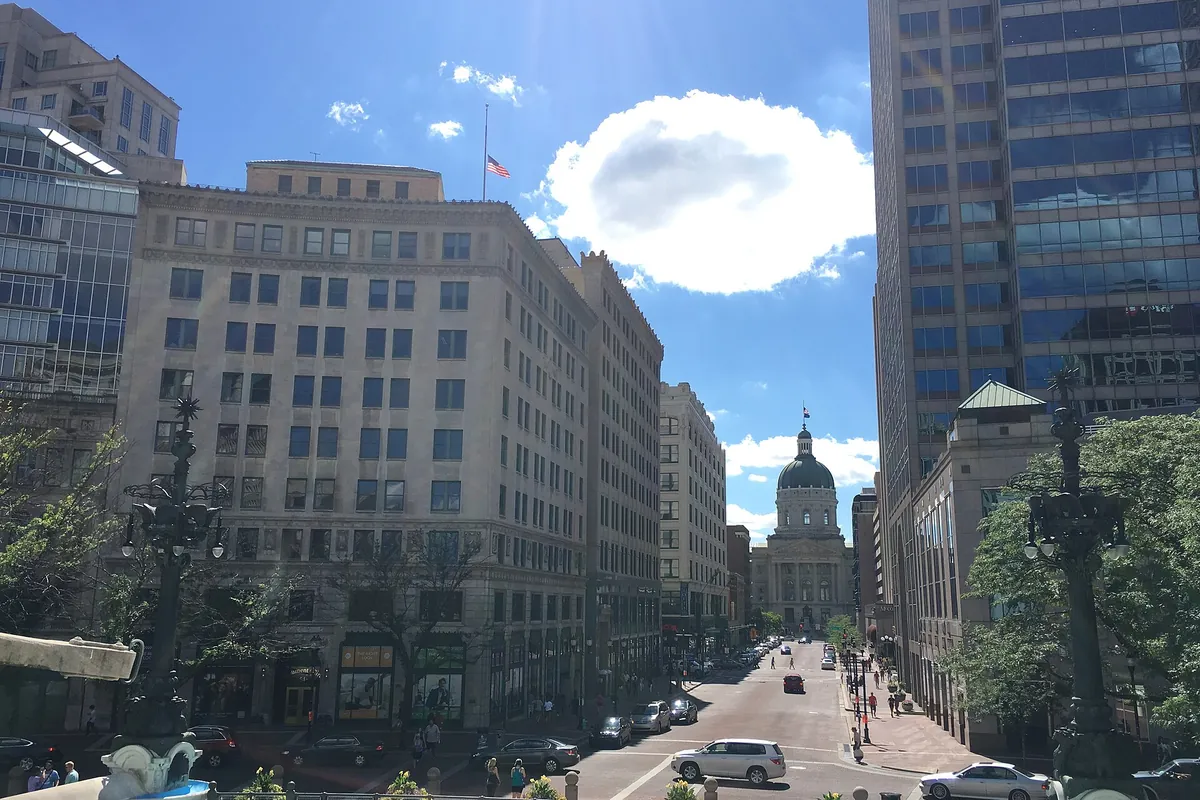 A downtown Indianapolis street lined with stone and glass office buildings under a summer sky