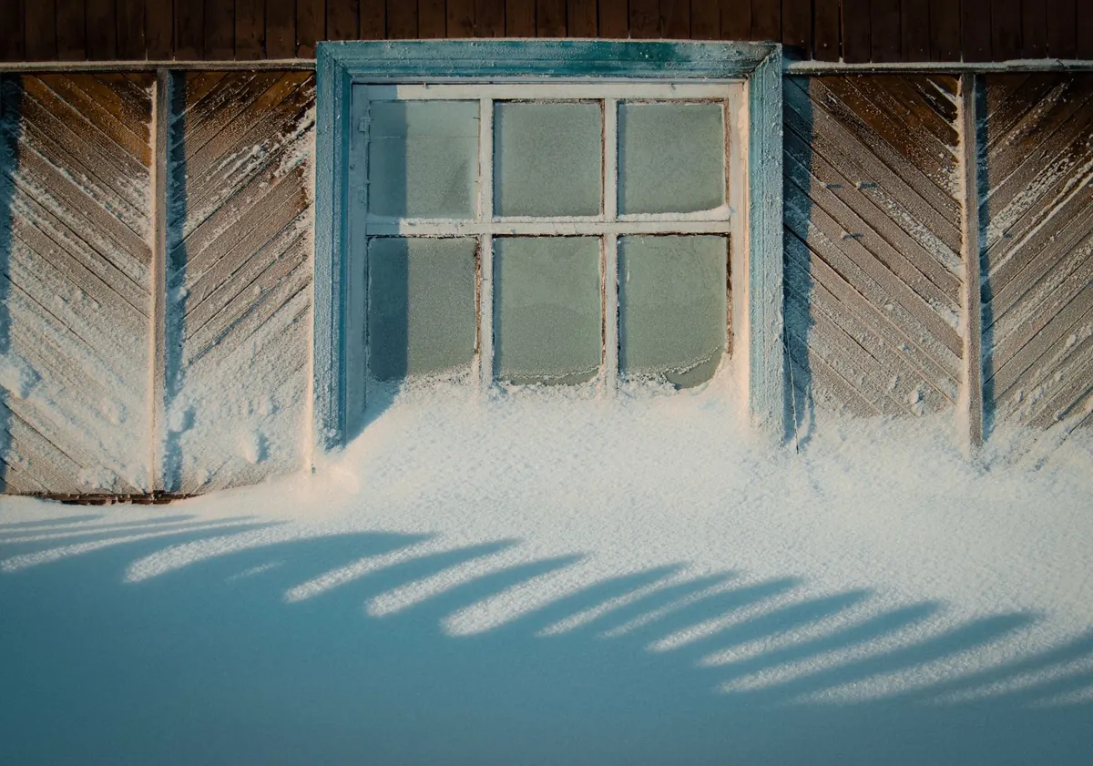 Snow drifted against the window of a wooden cabin