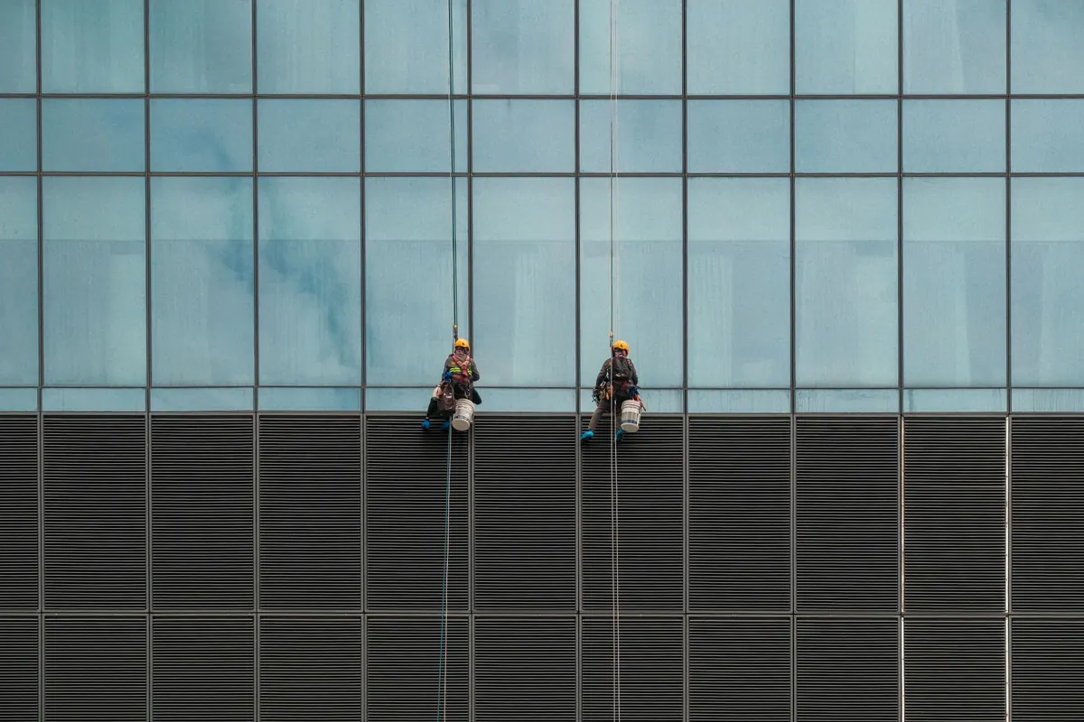 Two rope-access workers on a glass office facade