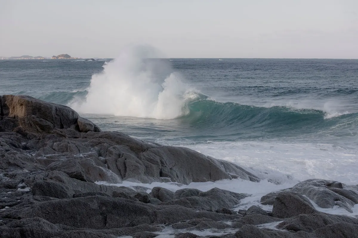 A wave breaking into spray on a rocky shore