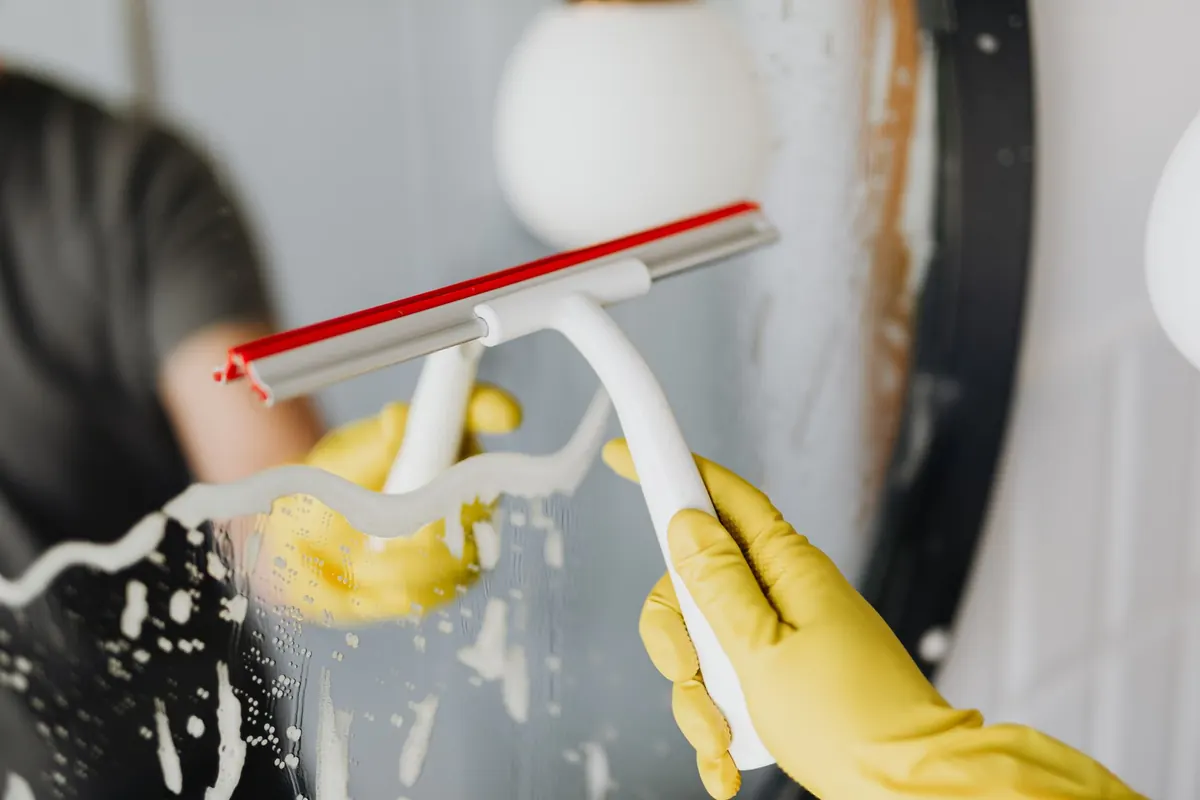 A gloved hand holding a squeegee blade against glass